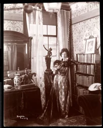 Anita Chartres staand in de hoek van een kamer, ca. 1898